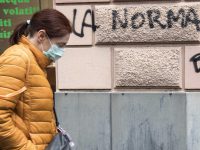 A woman wearing a protective mask walks next an inscription painted on  the wall of a building reading in italian "normality", Genoa, Italy, 21 April 2020. Italian Prime Minister Giuseppe Conte, during his speech to the Chambers, said that the masks and the social security distancing will be maintained until a vaccine against Covid-19 wil not be discovered. ANSA/LUCA ZENNARO