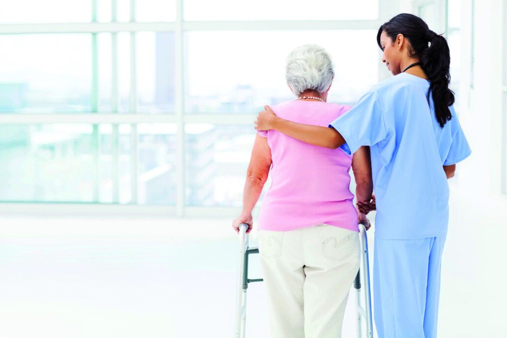 Rear view of female nurse assisting senior woman with walker in nursing home. Horizontal shot.